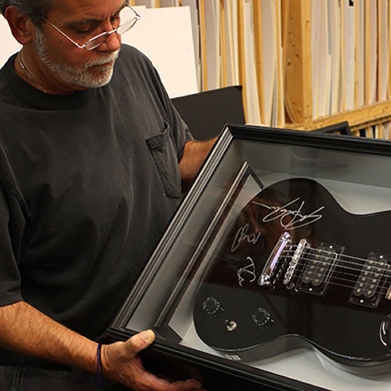 Bluegrass Frames framer holding a framed and signed guitar